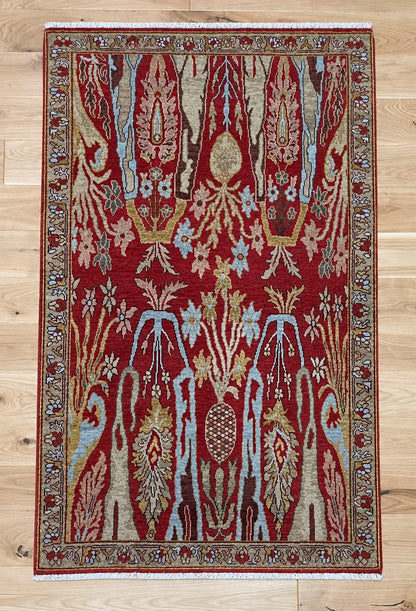 A rectangular area rug with a traditional ornate pattern in deep red, beige, light blue, and gold, laid flat on a light wood floor.