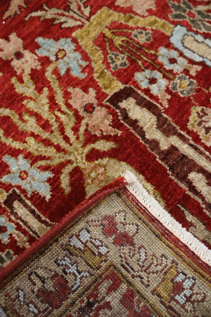 Close-up of a patterned area rug with a deep red field, beige and brown floral motifs, light blue flower accents, and a cream fringe along the corner.