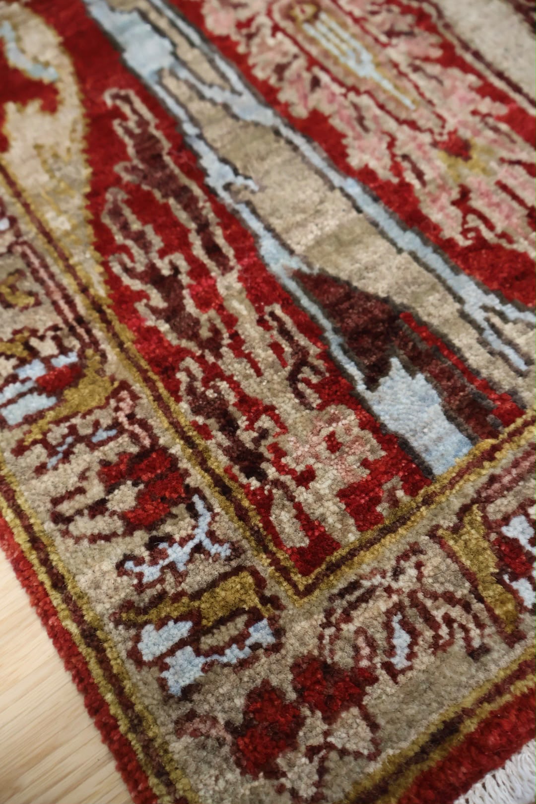 A close-up of a traditional patterned area rug with red, beige, and gold tones, showing the detailed woven texture and corner design.