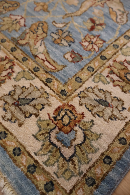 Close-up of a traditional patterned area rug corner showing a light blue field, beige border, and floral motifs in beige, rust, and muted green.
