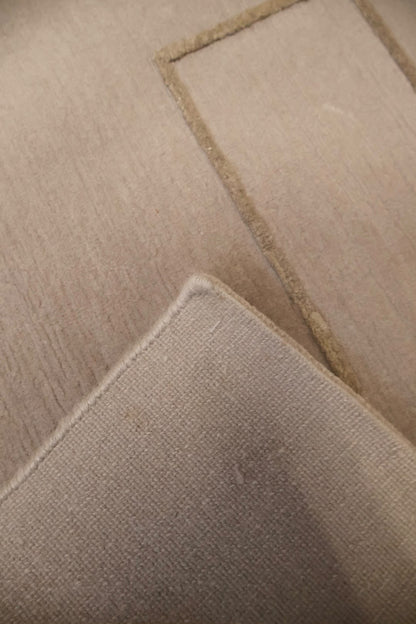 A close-up of a beige woven fabric with a stitched rectangular border and a folded corner showing the texture.