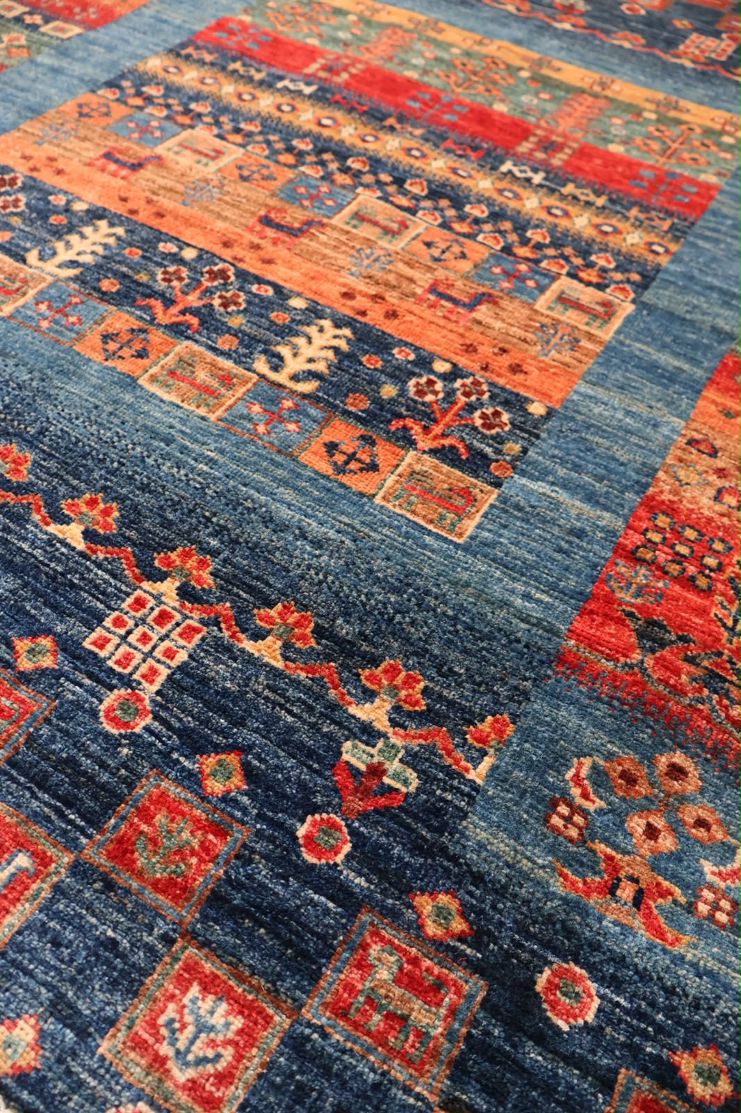 A close-up of a patterned area rug with a navy blue field, red and orange geometric borders, and cream floral motifs.