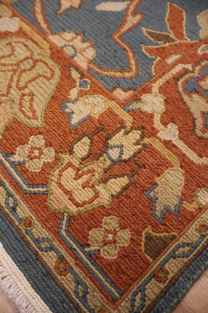 Close-up of a patterned area rug with a rust-orange field, beige floral motifs, and a muted blue border and background.