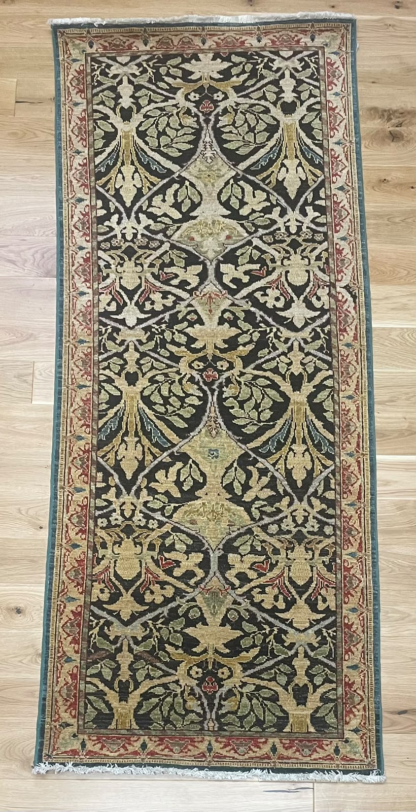 A rectangular vintage-style area rug with an intricate floral and vine pattern, displayed flat on a light-colored wooden floor.