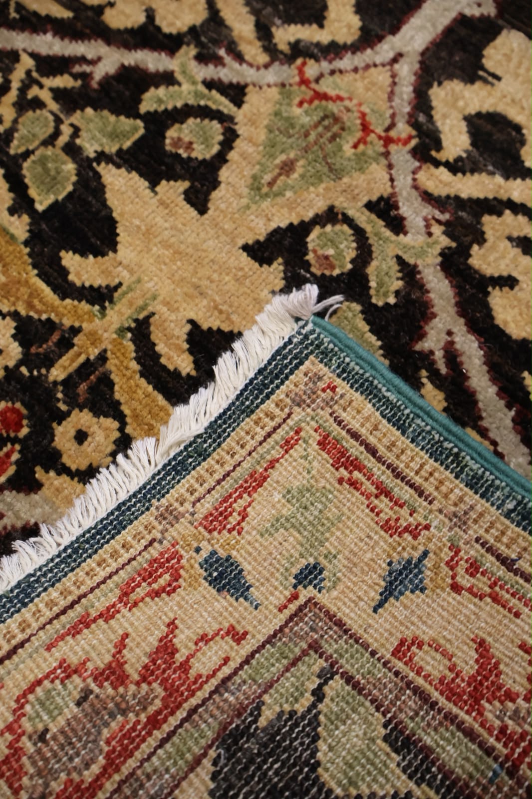 Close-up of a patterned area rug corner showing cream, black, red, green, and blue woven motifs with white fringe.