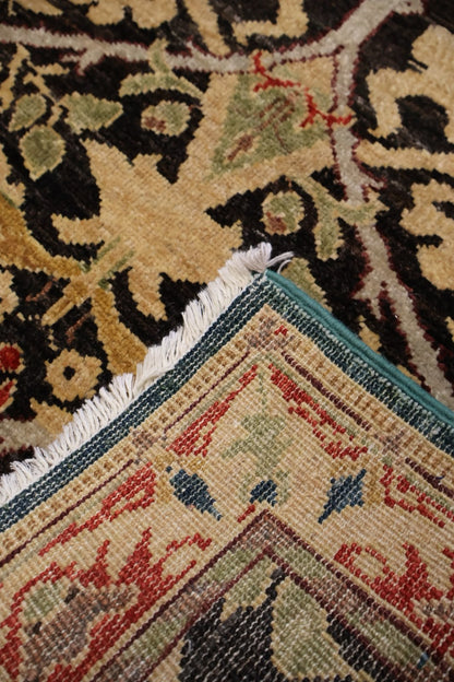 Close-up of a patterned area rug corner showing cream, black, red, green, and blue woven motifs with white fringe.