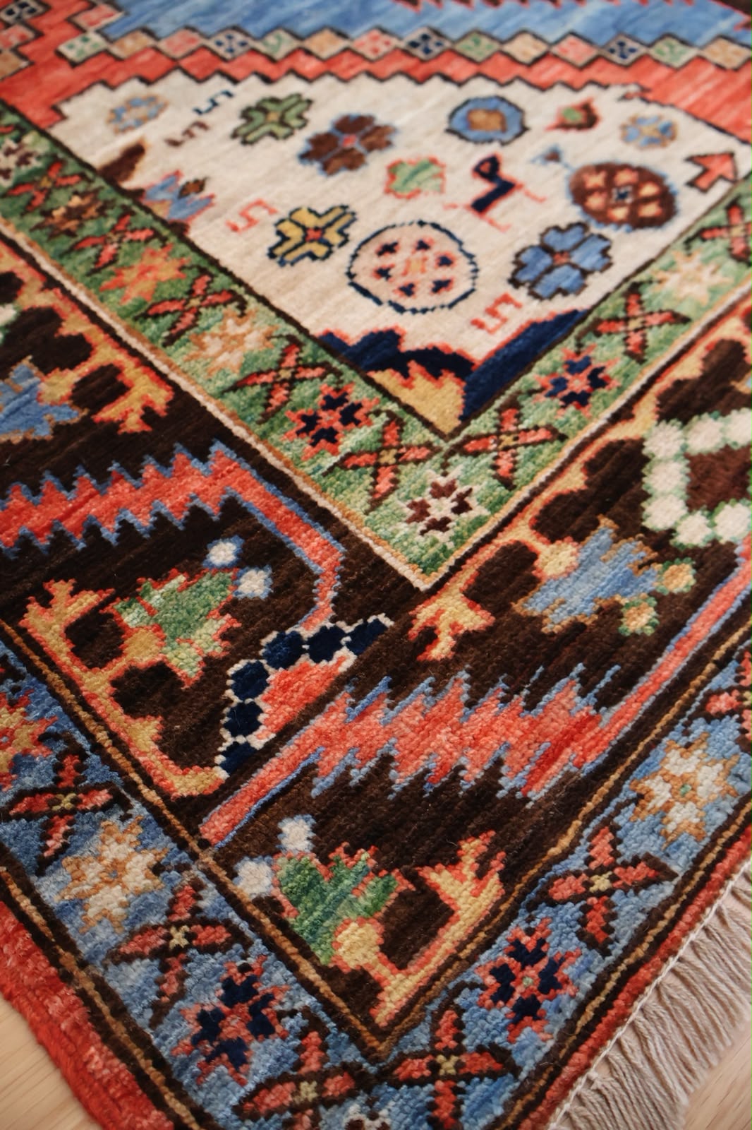 A close-up of a traditional patterned area rug with a cream field, a blue border, and dark brown sections with geometric and floral motifs.
