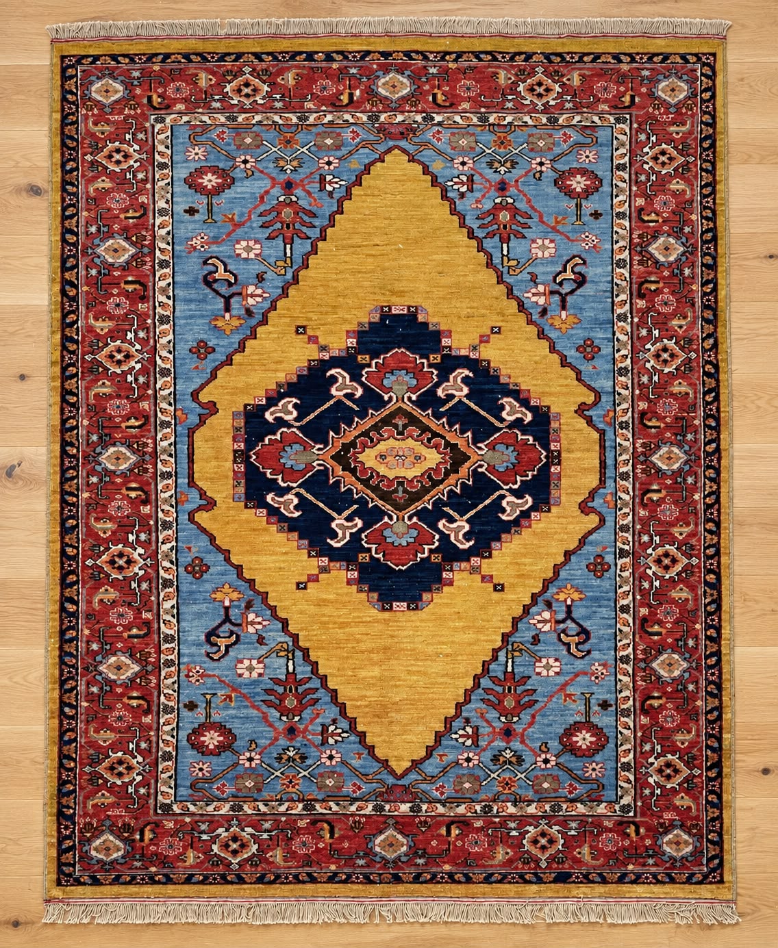 A traditional oriental-style area rug with a geometric pattern, featuring a large mustard yellow central diamond, a dark navy blue medallion, and a red border, laid flat on a light wood floor.