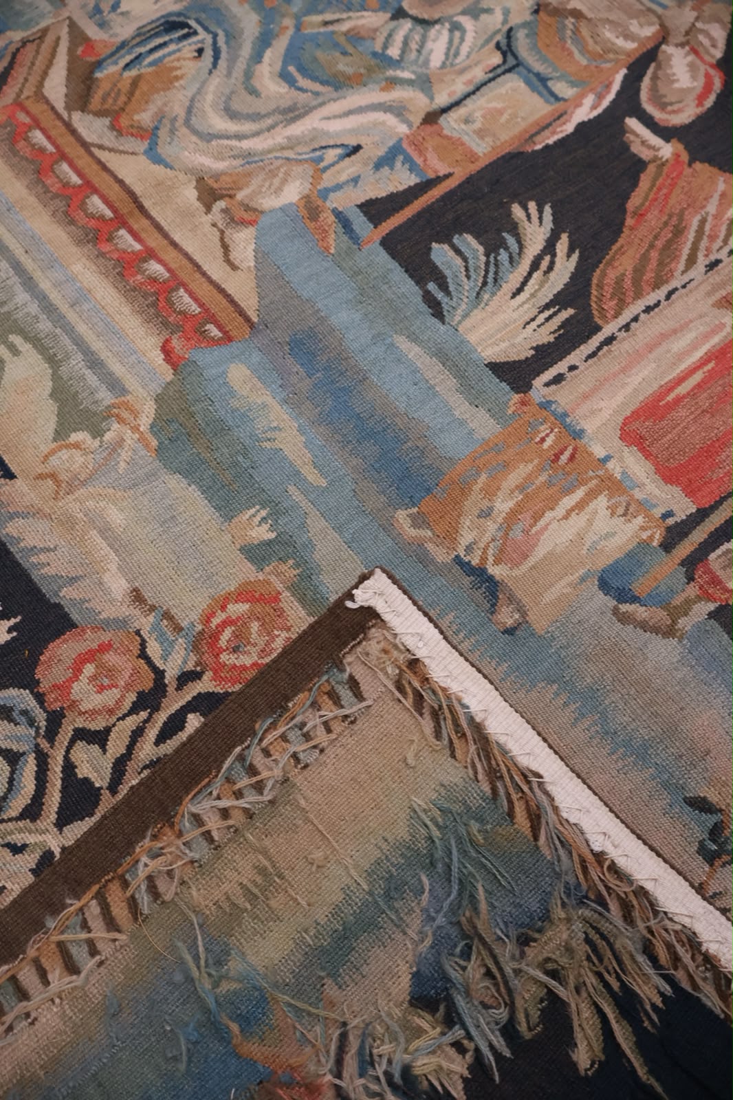 Close-up of a woven tapestry showing a detailed multicolor pattern with blue, beige, red, brown, and cream tones.