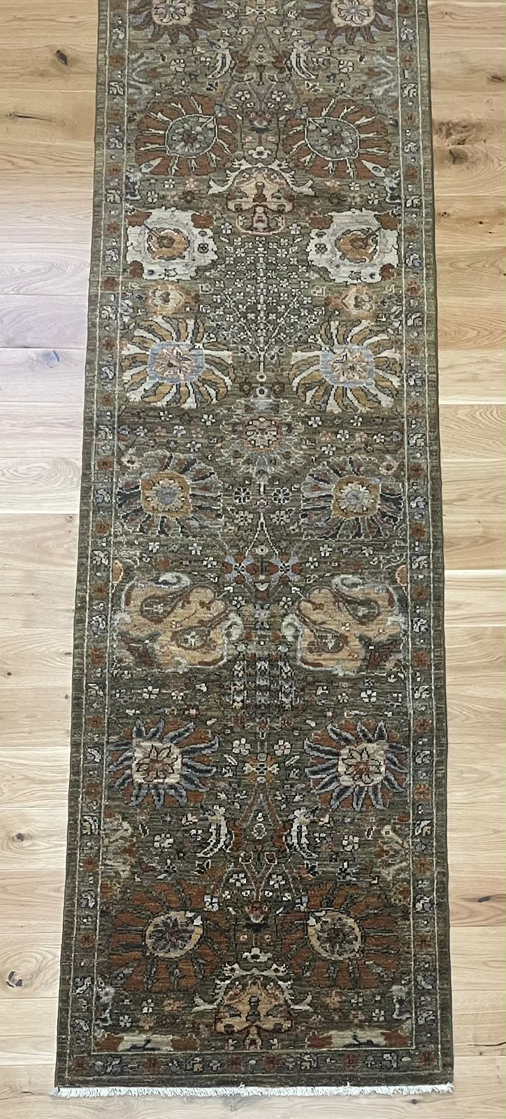 A long rectangular area rug with an intricate traditional floral and medallion pattern, shown laid out on a light-colored wooden floor.