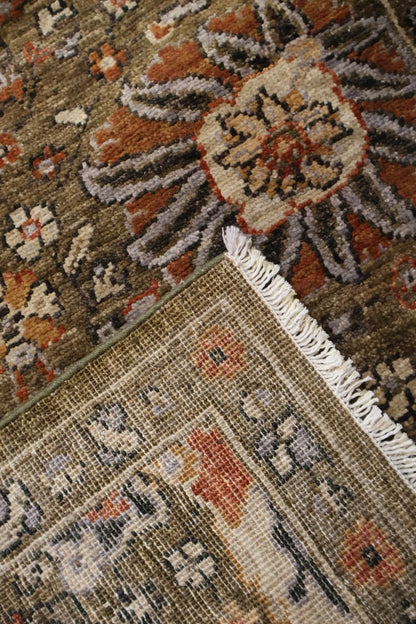 A close-up of a traditional patterned area rug showing its corner with white fringe, featuring a floral motif in earthy tones of brown, rust, beige, and gray.