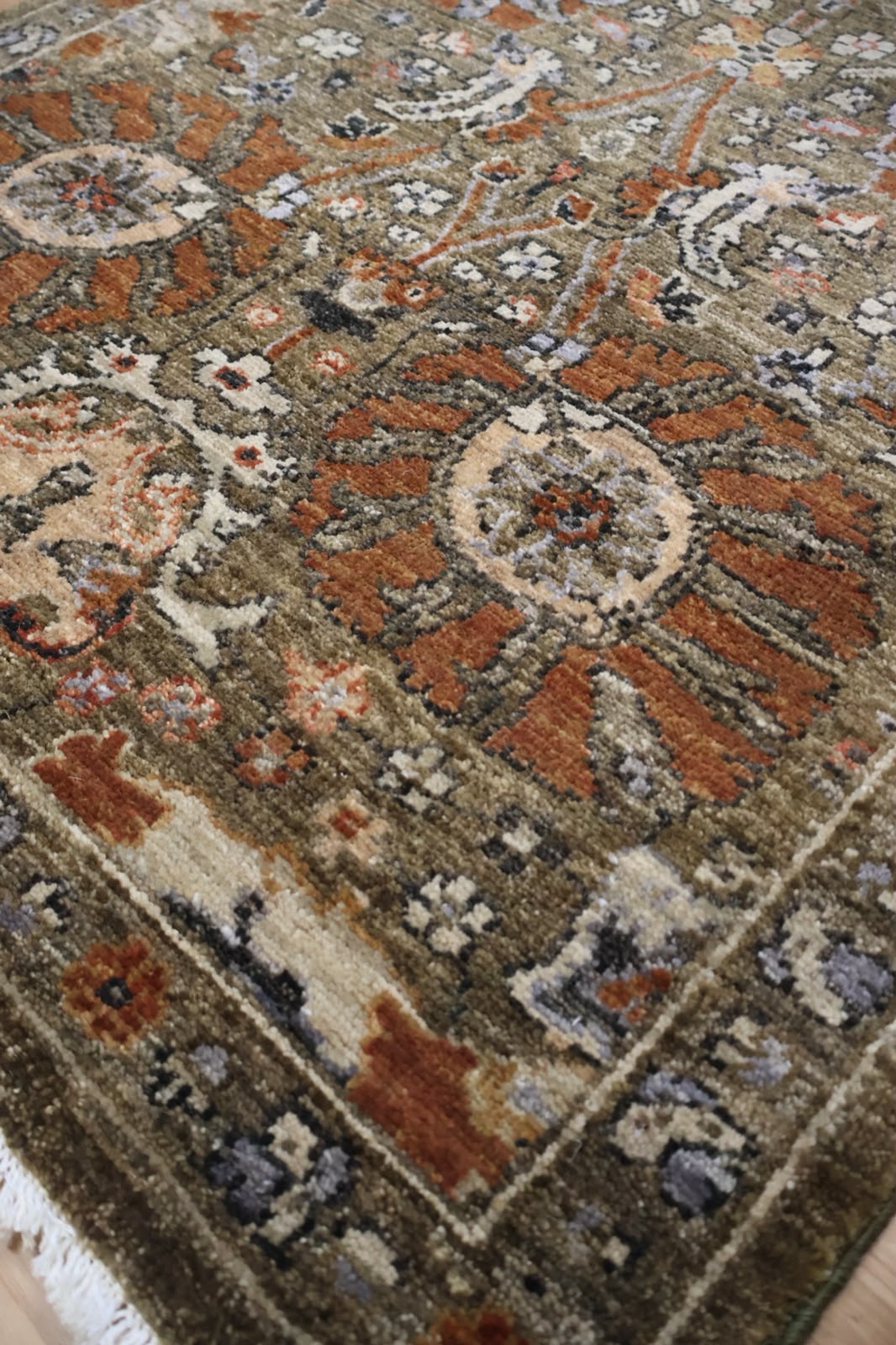 A close-up view of an ornate traditional area rug with a complex floral and medallion pattern in earthy tones of brown, rust orange, beige, and muted blue-gray.