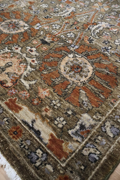 A close-up view of an ornate traditional area rug with a complex floral and medallion pattern in earthy tones of brown, rust orange, beige, and muted blue-gray.