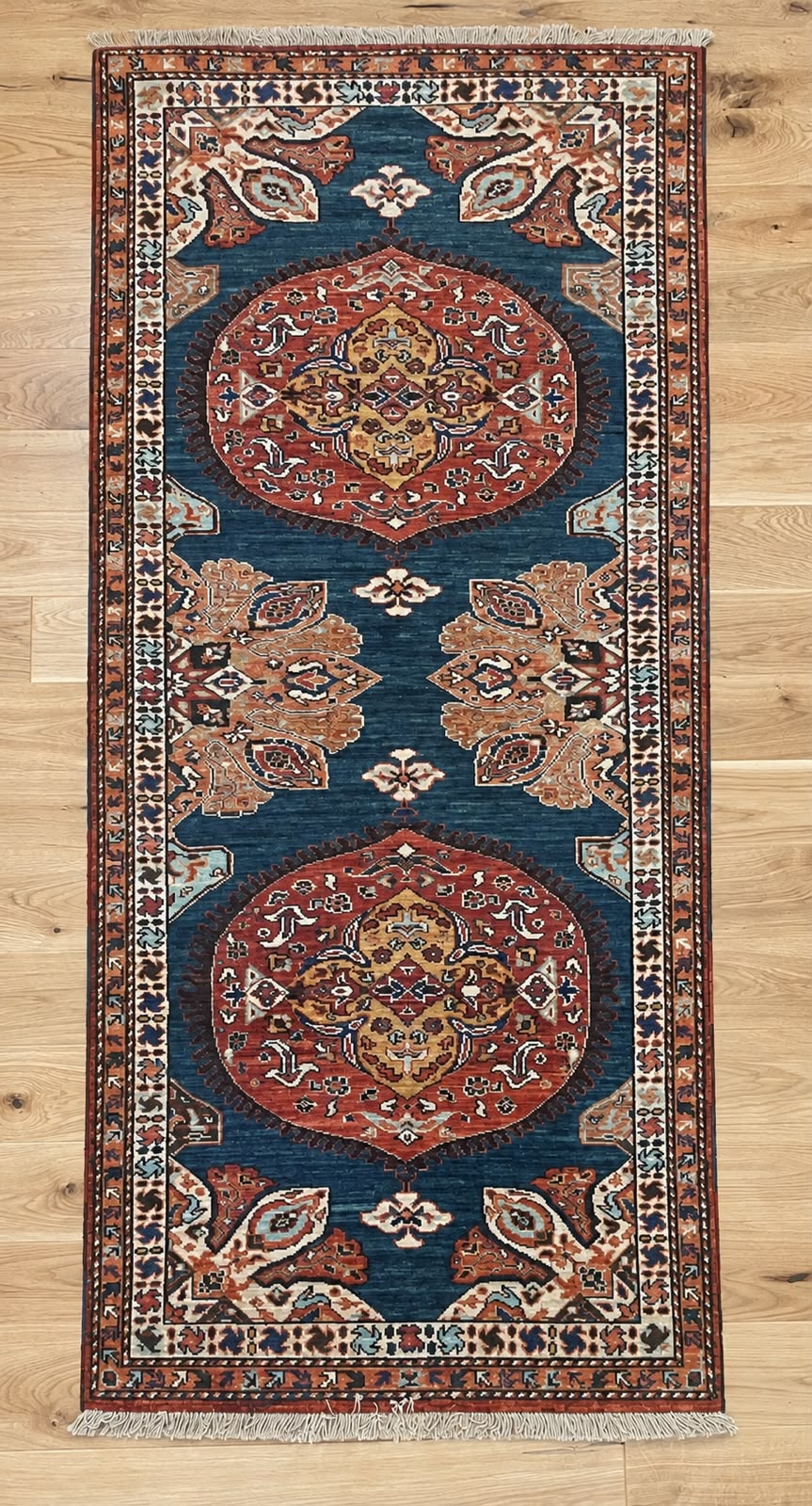 A traditional oriental runner rug with two large central medallions, displayed flat on a light wood floor.