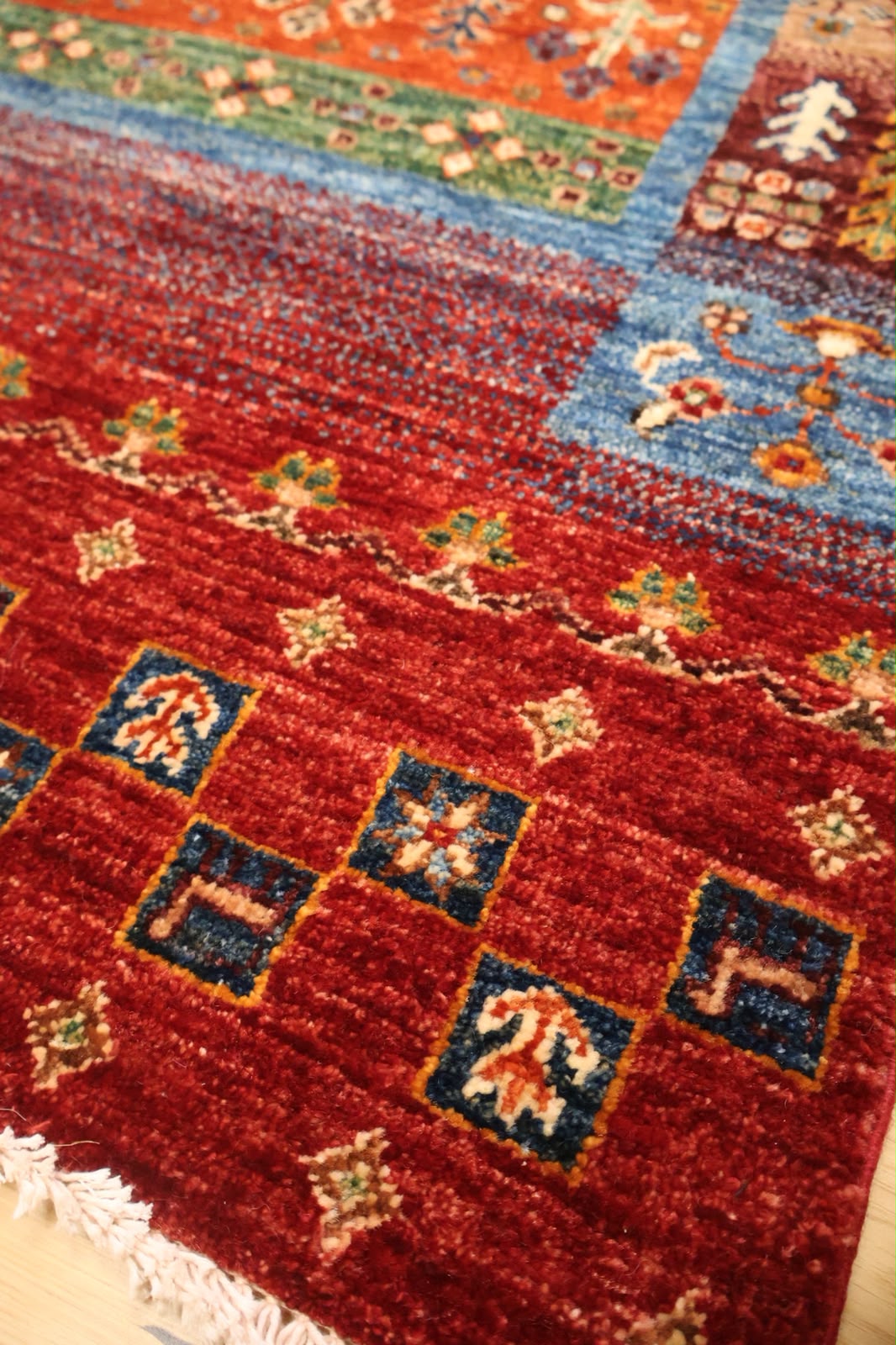 A close-up of a patterned area rug with a deep red field, blue borders, and small beige and green floral motifs.