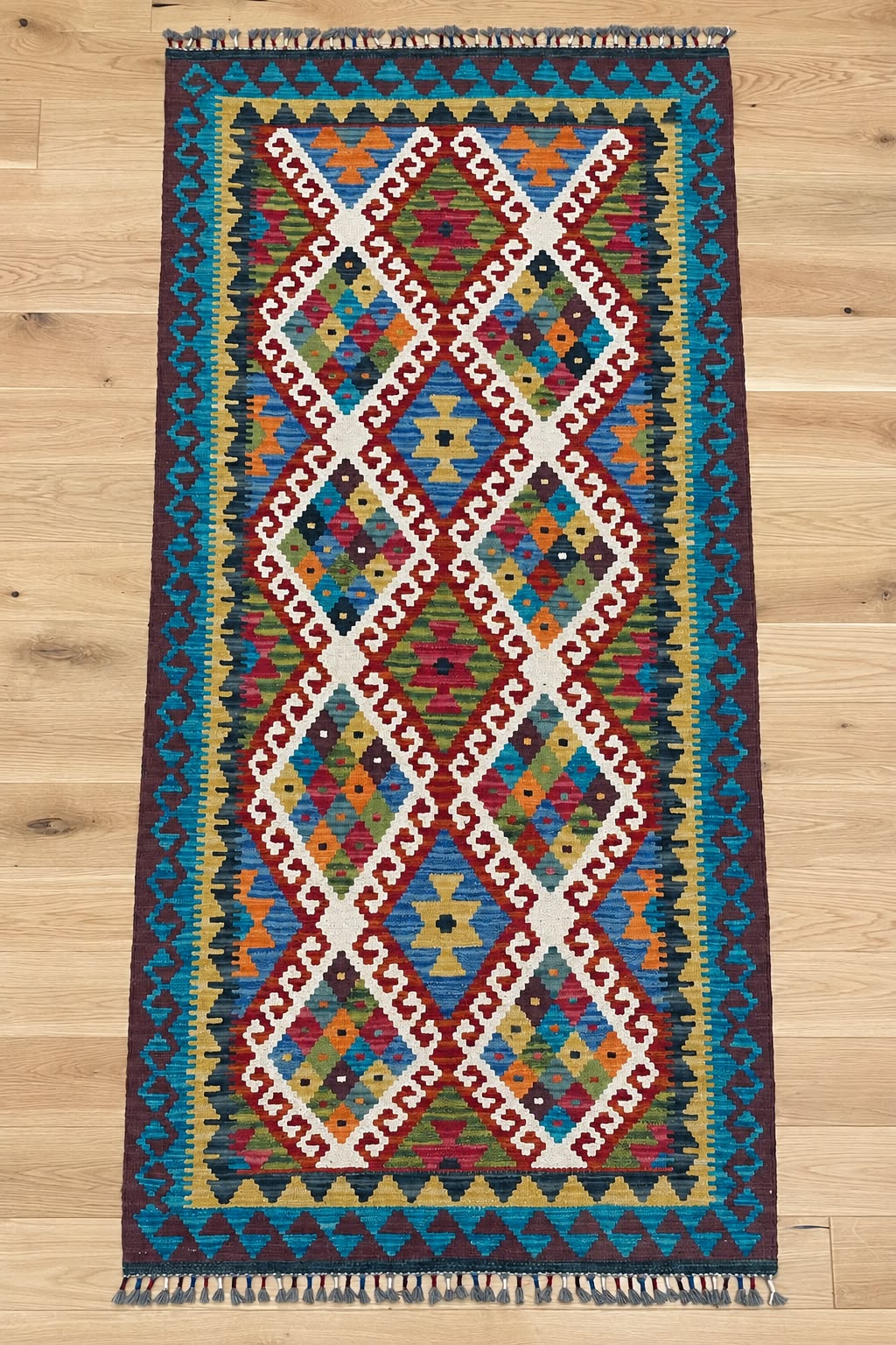 A long rectangular kilim runner rug with a vibrant geometric diamond pattern, displayed flat on a light wood floor.